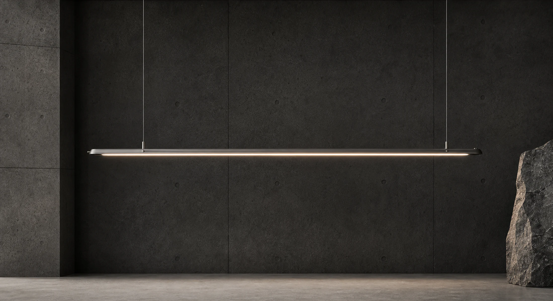 A slim linear lamp held by two tension cables against a dark concrete wall