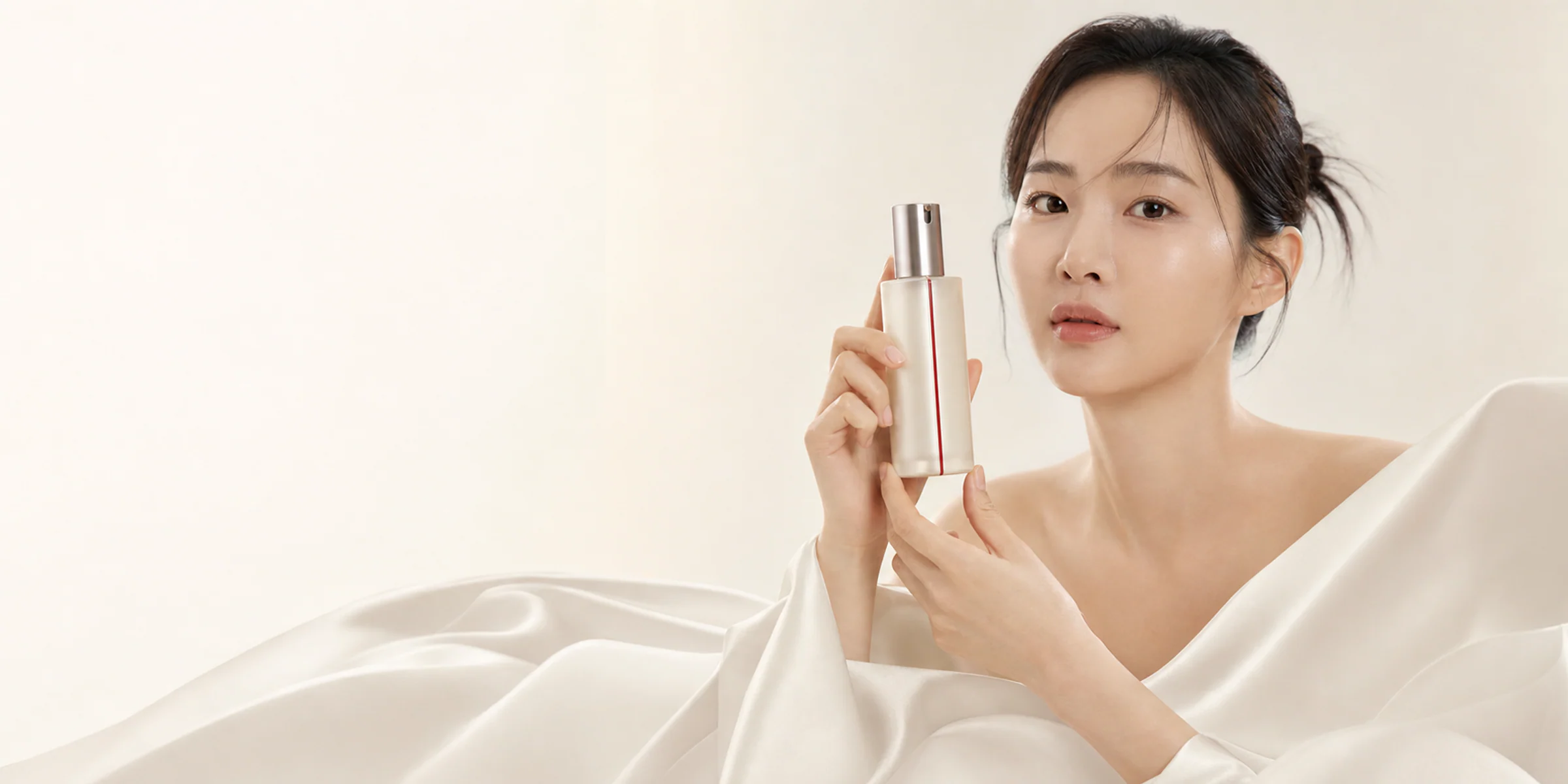 KINUVE bottle held beside ivory silk folds