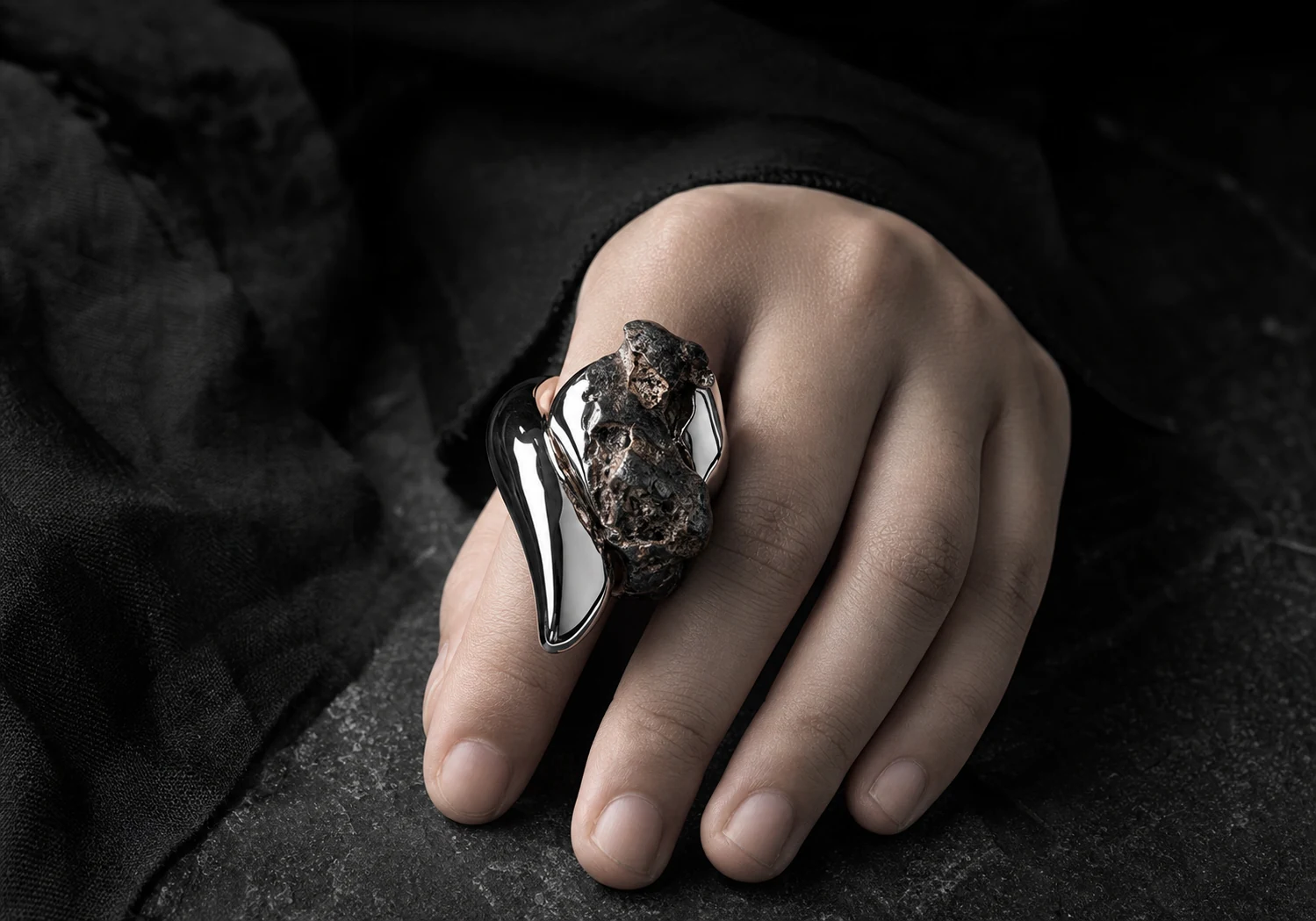 Sculptural ring worn on a hand over black fabric.