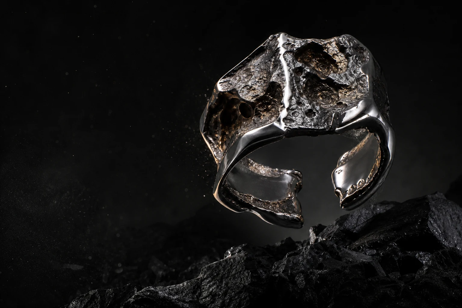 A sculptural mirror chrome and oxidized bronze cuff ring floating above black stone.