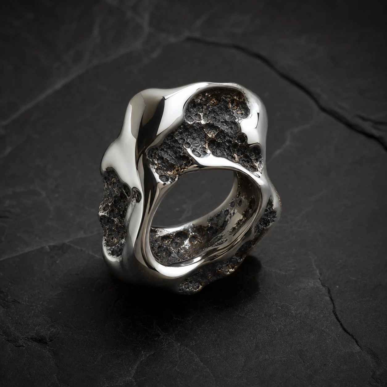 Molten Ring sculptural mirror chrome ring on black stone.